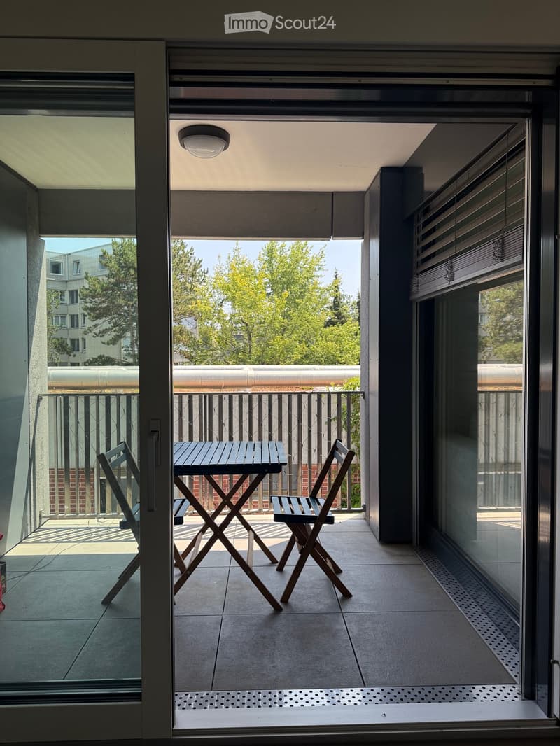 Balcony with a small table and two chairs, overlooking a green area with trees.