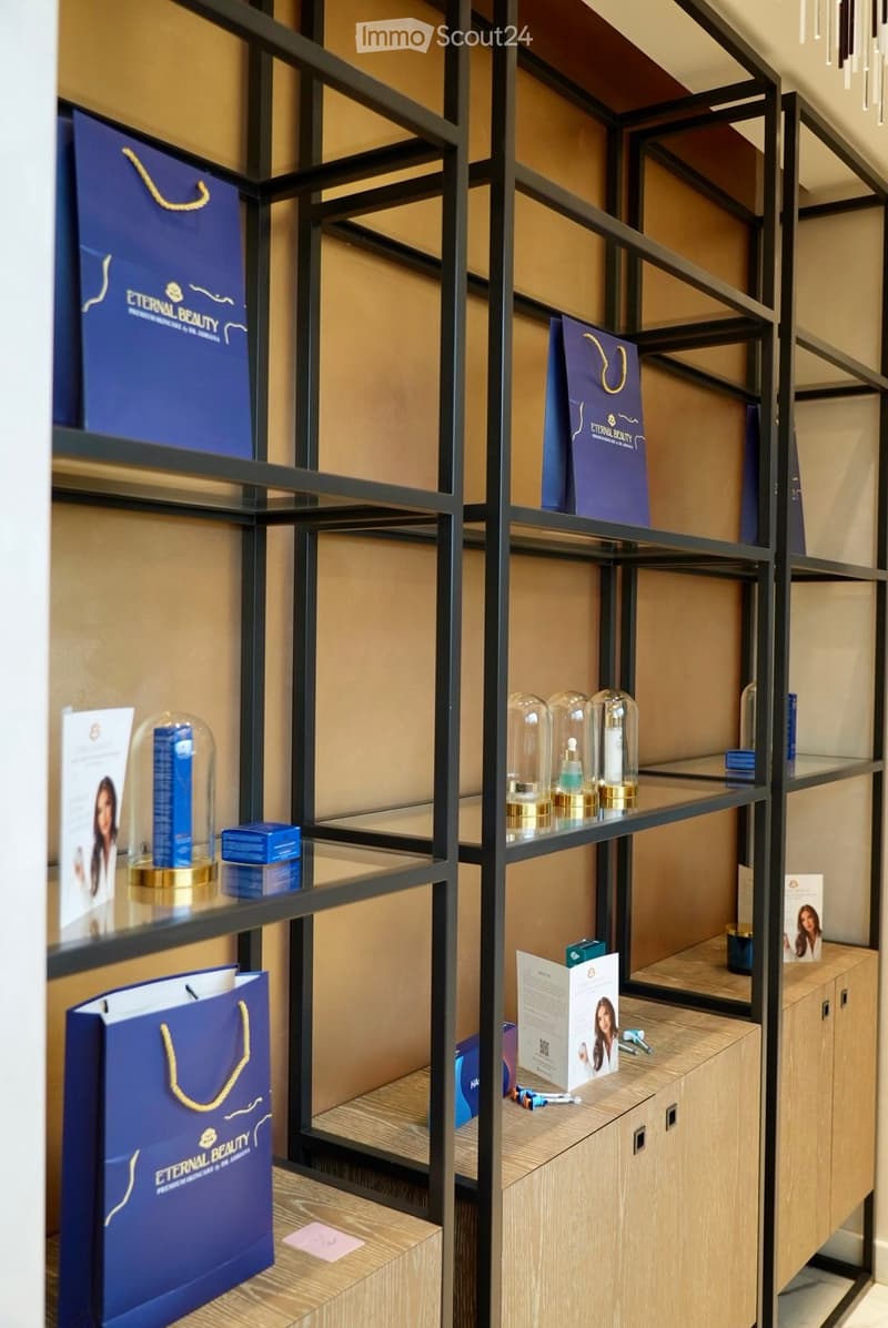 A modern, well-organized display area with shelves holding branded handbags, cosmetic bottles, brochures, and a small cabinet.