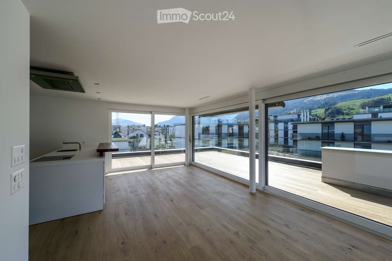 Bright, open-plan room with wooden flooring, large glass sliding doors leading to a balcony, and a scenic mountain view.