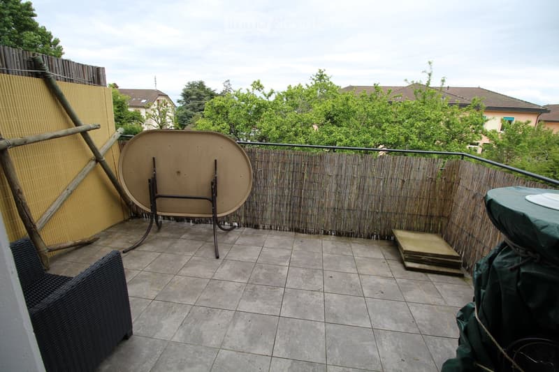 Balcony with tiled floor, bamboo fence, and outdoor furniture including a chair and a table.