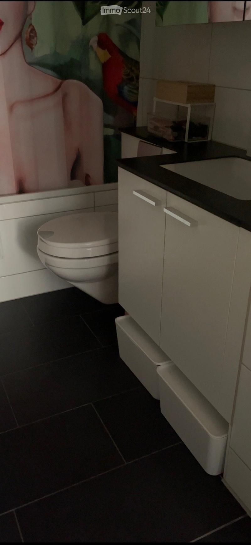 Modern bathroom with a toilet, sink, and cabinet. Dark tiled floor and light-colored cabinetry.