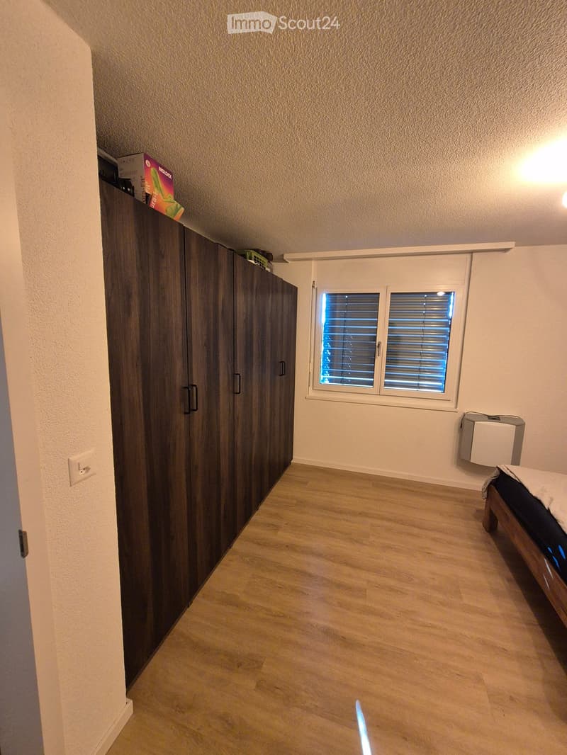 Bedroom with wooden floor, large wardrobe, bed, window with blinds, and a radiator.