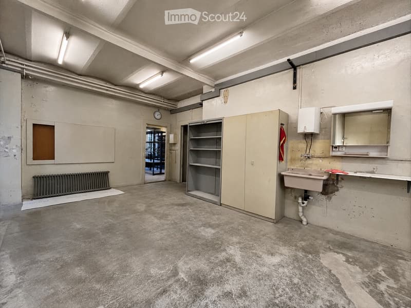 Empty room with concrete floor, exposed pipes, sink, cabinets, and a radiator. No furniture or personal items present.