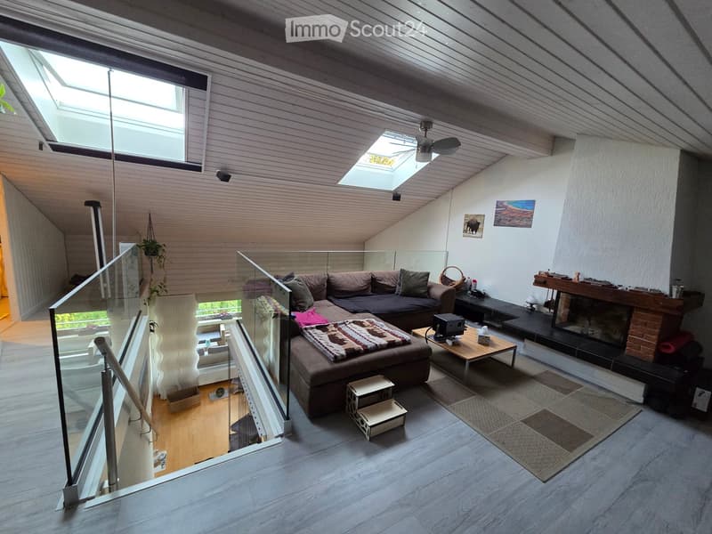 Modern living room with a sectional sofa, coffee table, fireplace, and large windows. Features a glass railing and skylight.