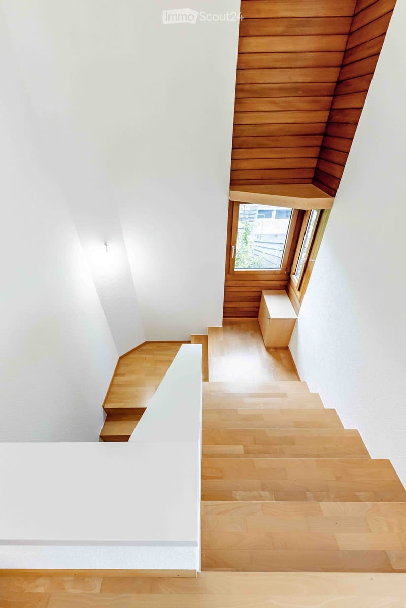 Modern staircase with wooden steps and white walls, featuring a small window at the top landing.