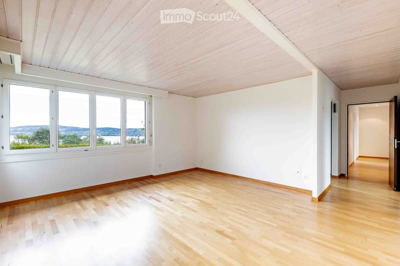 Empty room with light wooden flooring, white walls, and large windows offering a scenic view. No furniture or equipment present.