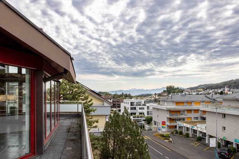 Balcony overlooking a residential area with buildings, trees, and distant mountains under a partly cloudy sky.