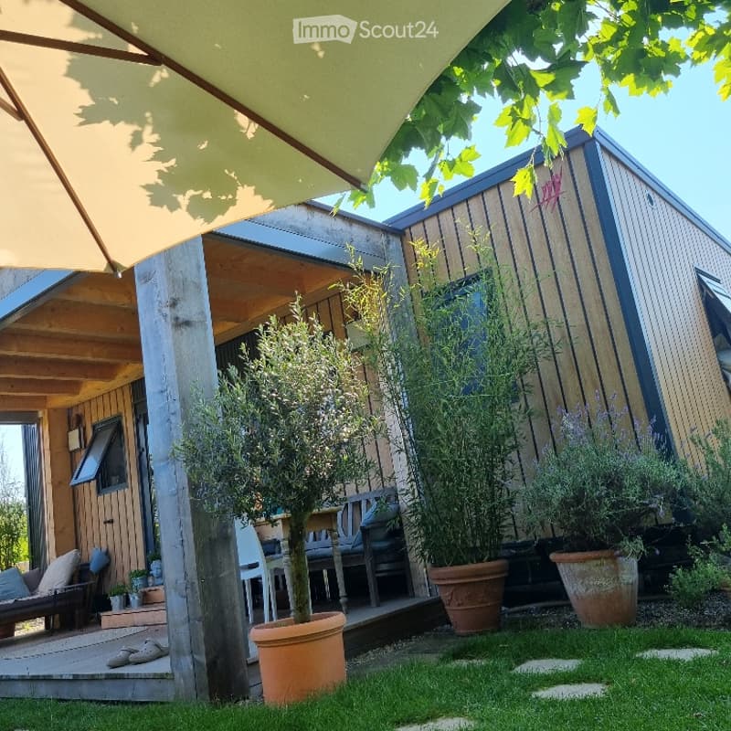 A well-maintained garden area with potted plants, a wooden deck, and outdoor furniture, including a bench and chairs.