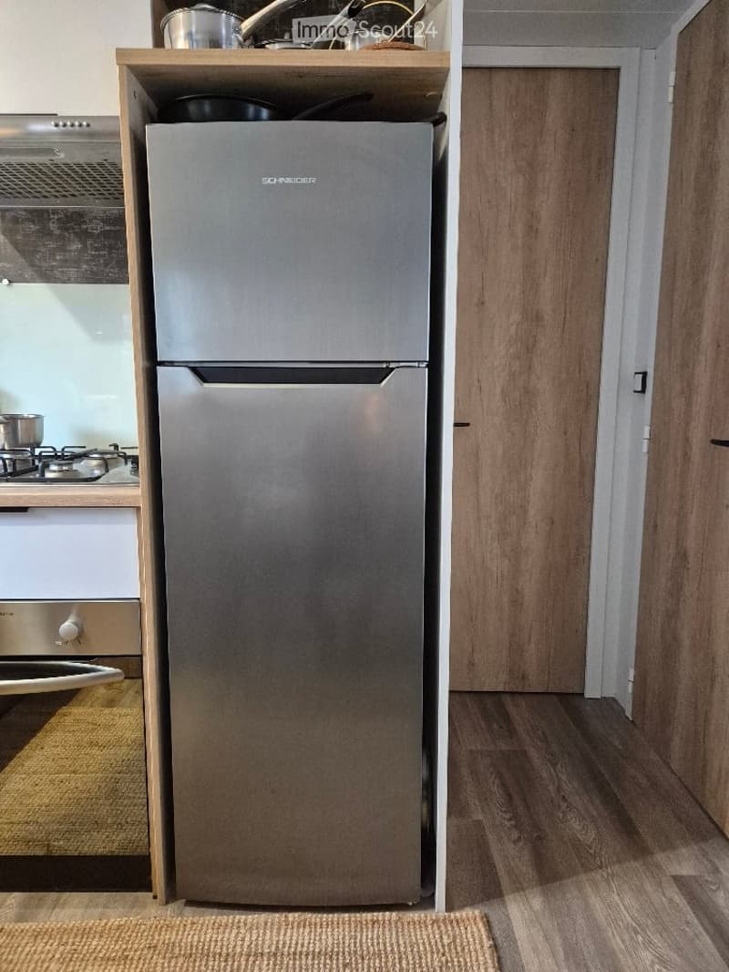 Modern kitchen with a stainless steel refrigerator, gas stove, and wooden shelves holding pots and pans.