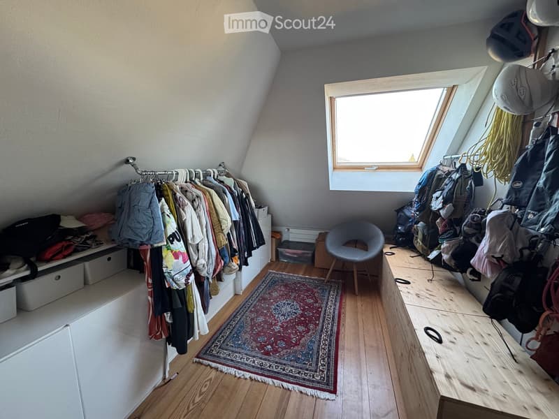 Attic room with wooden flooring, slanted ceilings, skylight window, clothing rack, chair, storage boxes, and backpacks.