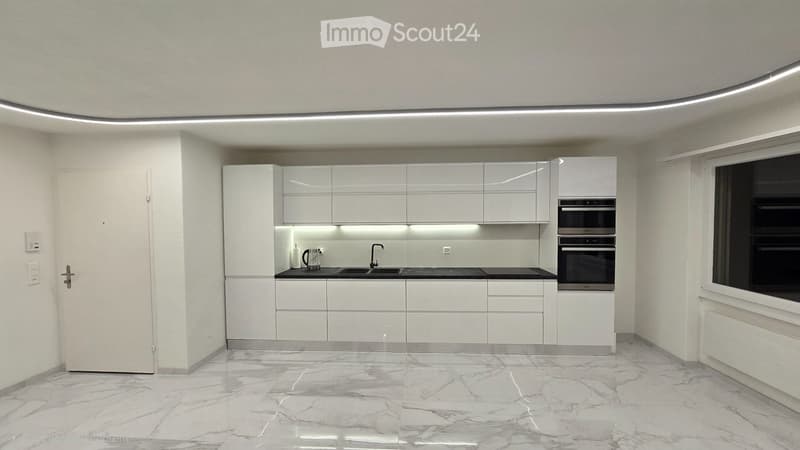 Modern, minimalist kitchen with white cabinets, marble flooring, and built-in appliances including a double oven and a coffee maker on the counter.
