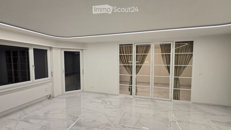 Empty room with white walls, marble flooring, large windows, and sliding glass doors with curtains.