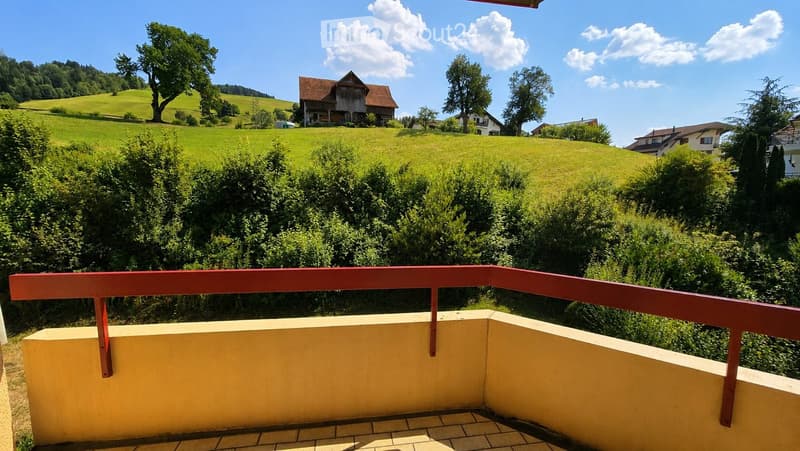 Balcony with a view of a green, hilly landscape, featuring a red railing and yellow walls.