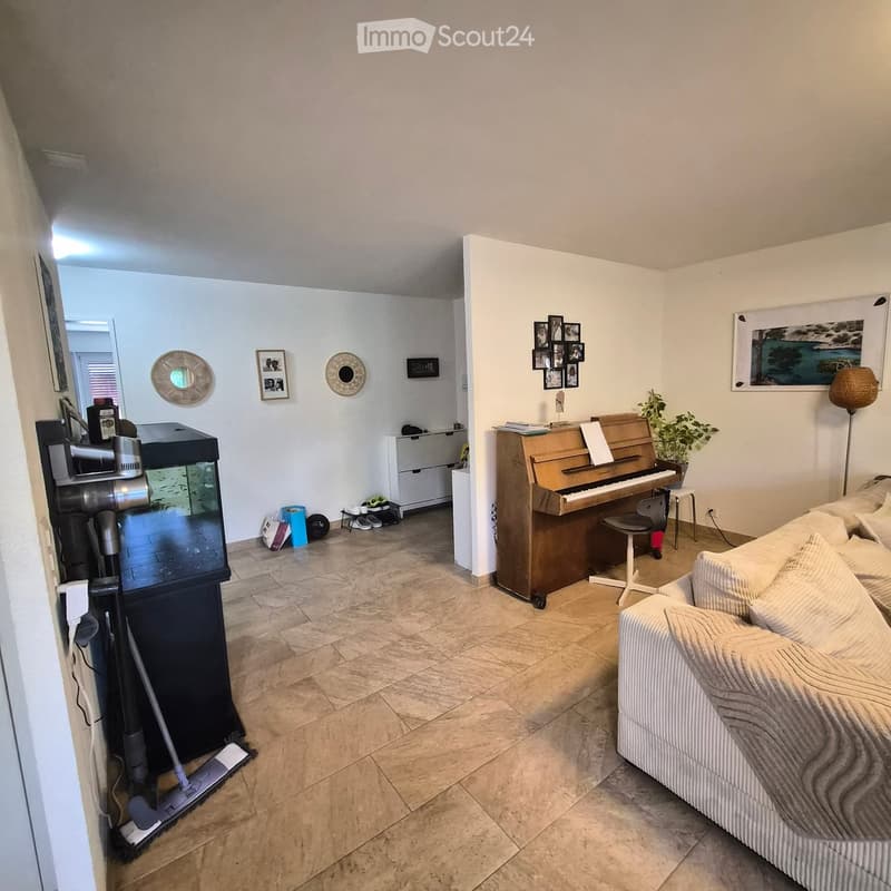 Living room with a sofa, piano, fish tank, and decorative items. The space features tiled flooring and white walls.