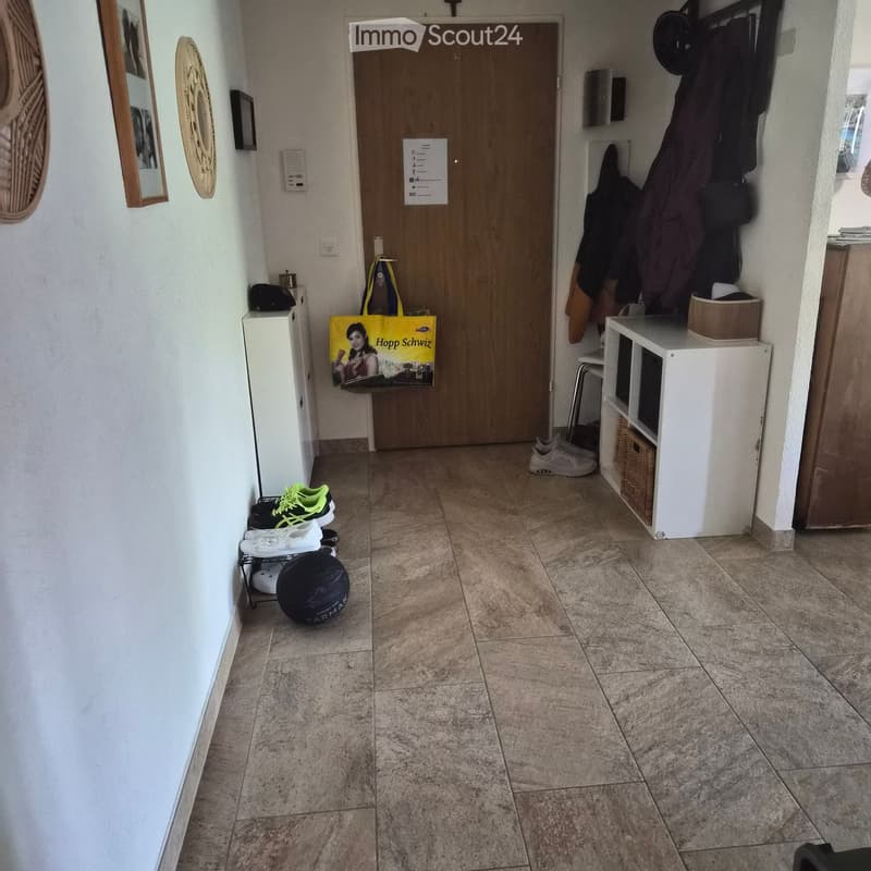 Hallway with tiled floor, coat rack, shoe rack, and a door leading to another room.