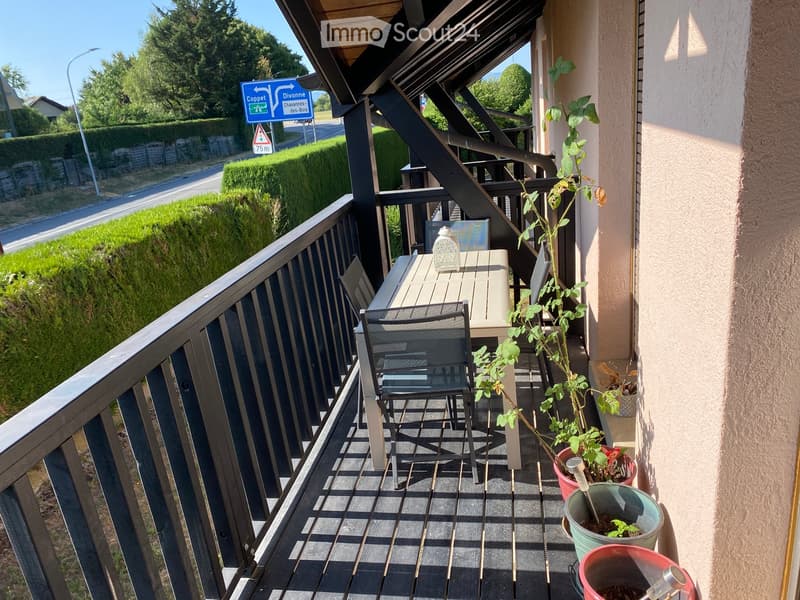 Balcony with wooden decking, metal railing, table, chair, and several potted plants.