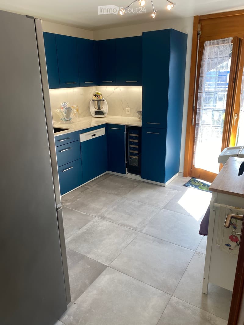 Modern kitchen with blue cabinets, white countertops, and stainless steel appliances. Features include a refrigerator, dishwasher, blender, and a sink.