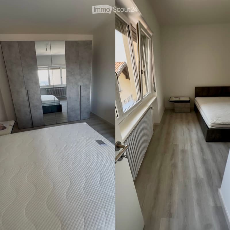 Modern bedroom with a large bed, a mirrored wardrobe, and a nightstand near the window. The room features light-colored wooden flooring and large windows allowing natural light.
