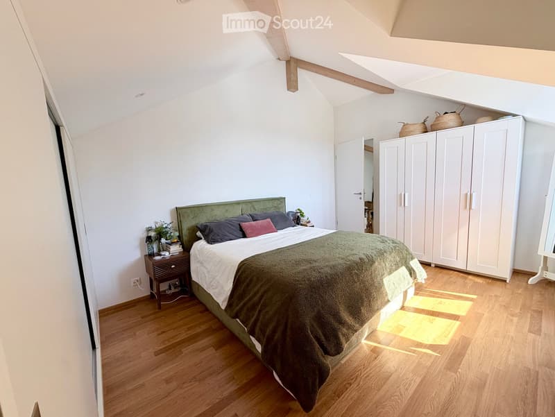 Cozy attic bedroom with wooden floors, slanted ceilings, a large bed with green headboard, nightstand, and built-in wardrobes.