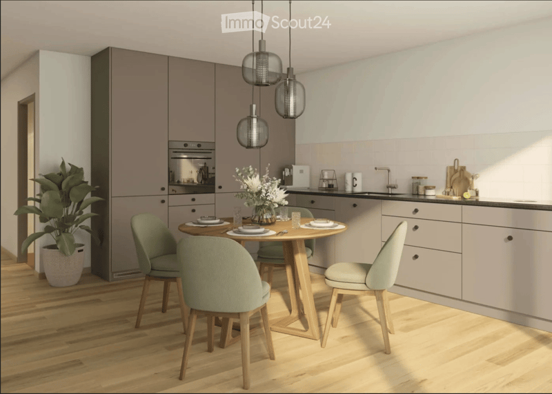 Modern kitchen with light-colored cabinets, a round wooden dining table with four green chairs, a potted plant, and a vase with flowers on the counter.