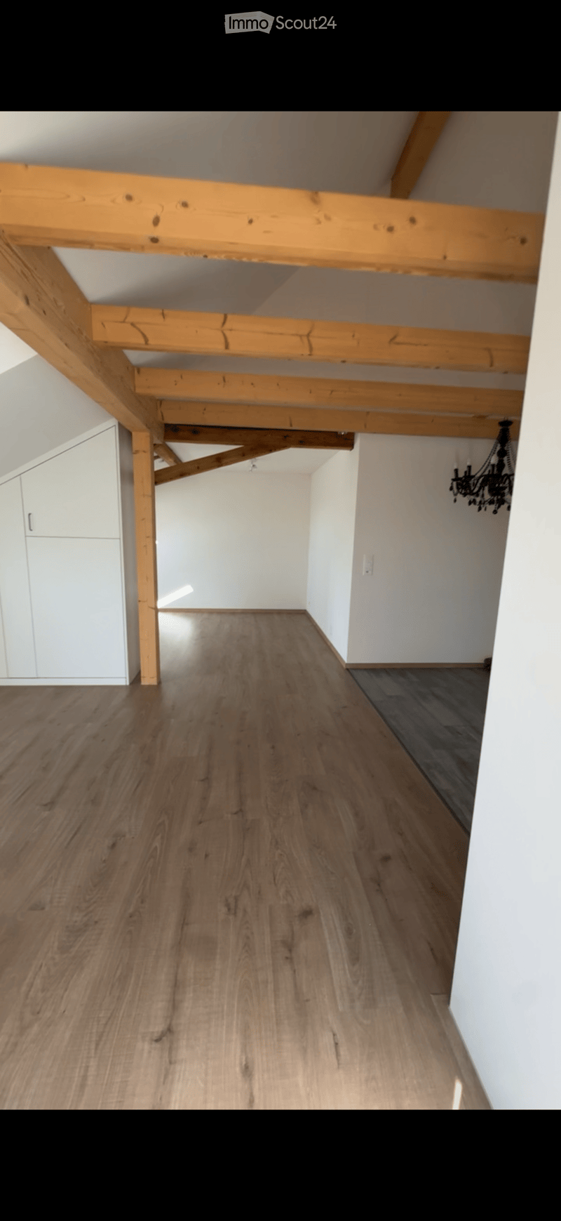 Empty room with wooden flooring, white walls, exposed wooden beams on the ceiling, and a white cabinet on the left side.
