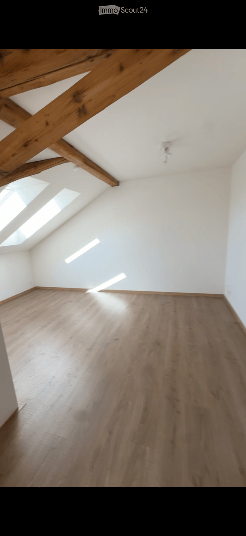Empty room with wooden floor and exposed wooden beams on the ceiling. Natural light streams in from skylights.