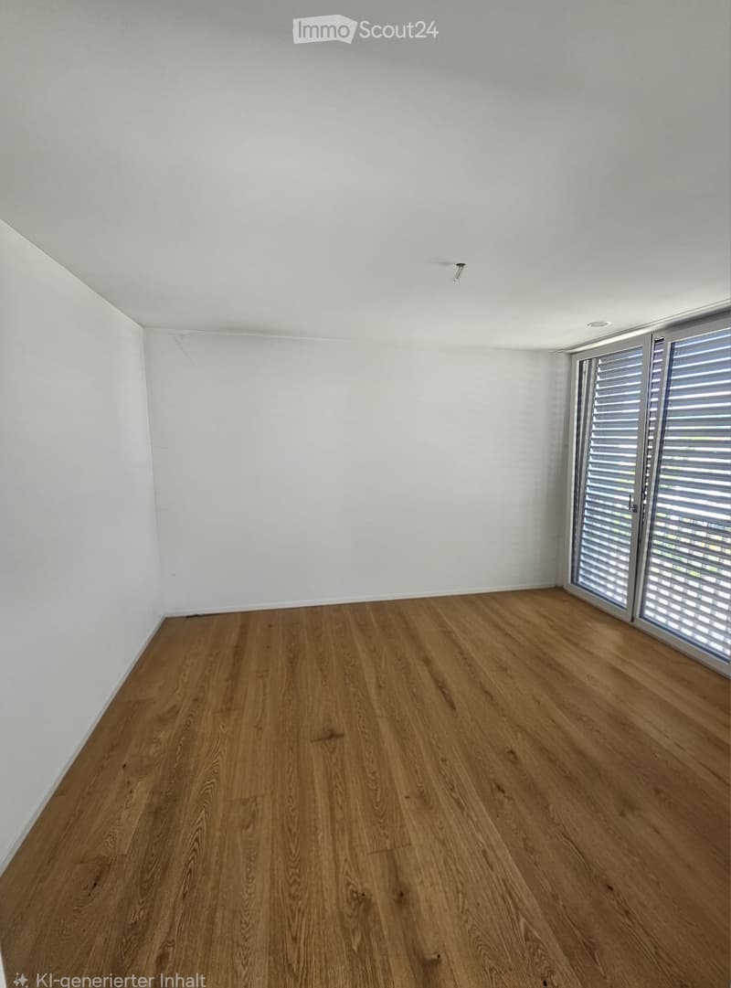 Empty room with wooden flooring and white walls, featuring large windows with blinds on the right side.