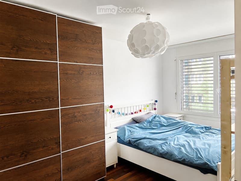 Modern bedroom with a white bed, blue bedding, a wooden wardrobe, and a round pendant light.