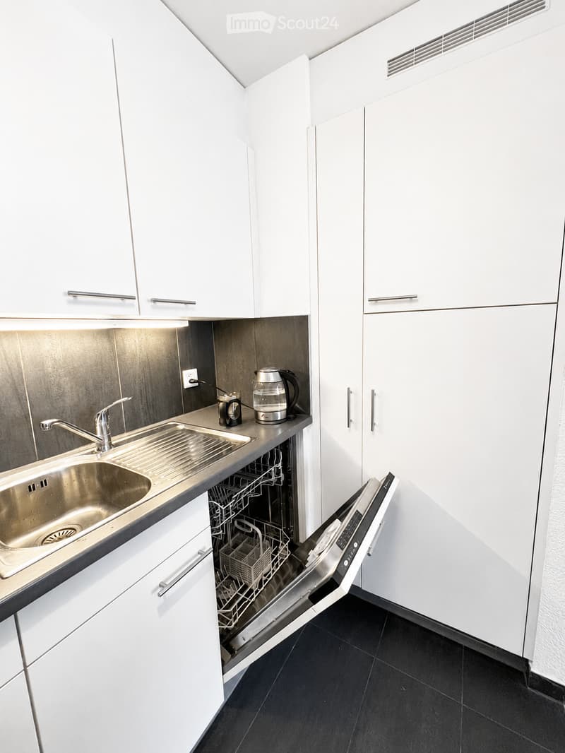 Modern kitchen with white cabinets, stainless steel sink, dishwasher, coffee maker, and electric kettle on the counter.