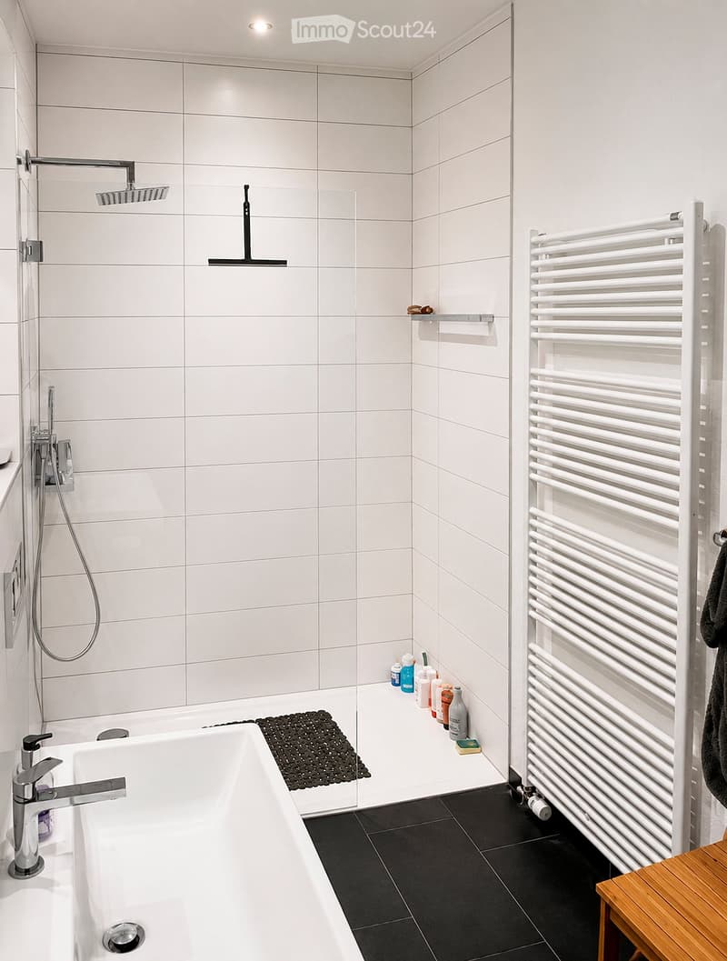 Modern bathroom with a white bathtub, chrome faucet, showerhead, radiator, and various toiletries on the shelf.