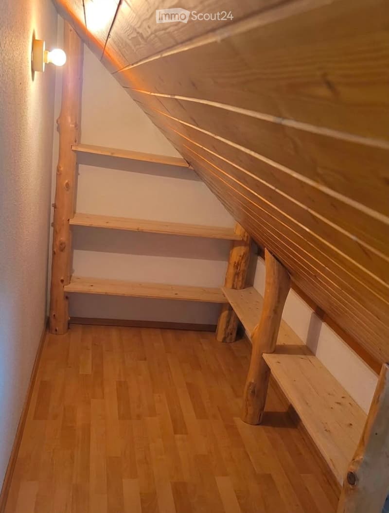 Empty wooden hallway with built-in wooden shelves and a slanted wooden ceiling. The walls are white, and the floor is made of light wooden planks.