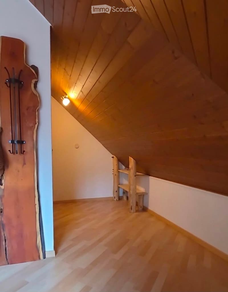 Empty attic room with wooden floors, slanted wooden ceiling, and built-in wooden shelving unit.