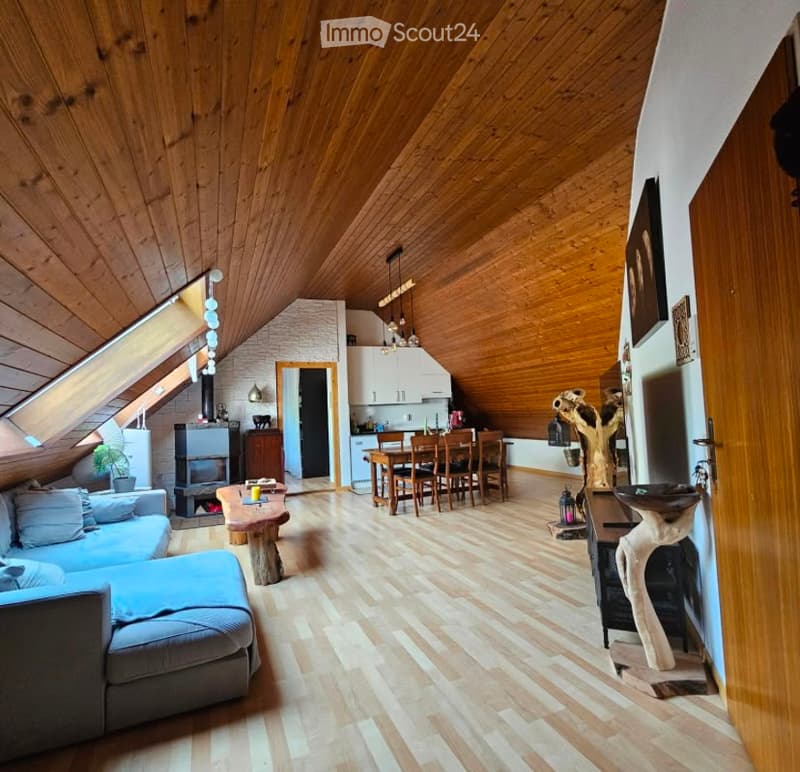 Open-plan living and dining area with wooden ceiling and floor, fireplace, sofa, coffee table, dining table with chairs, and kitchen area with cabinets.