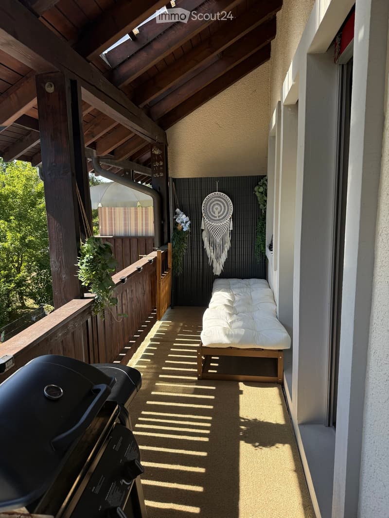 Balcony with a wooden slatted roof, a daybed, a dreamcatcher, and potted plants.