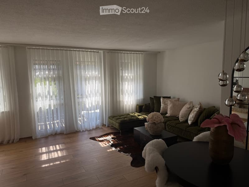 Modern living room with a green sofa, coffee table, bench, decorative vases, and a patterned rug on a wooden floor.