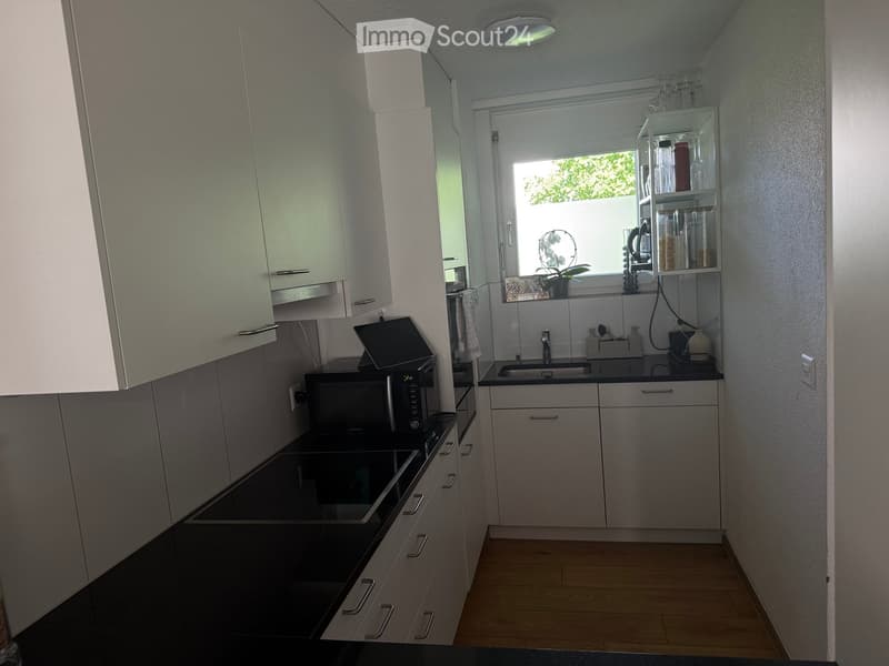 Modern kitchen with white cabinets, black countertops, microwave, fridge, sink, and shelves with glassware and containers.