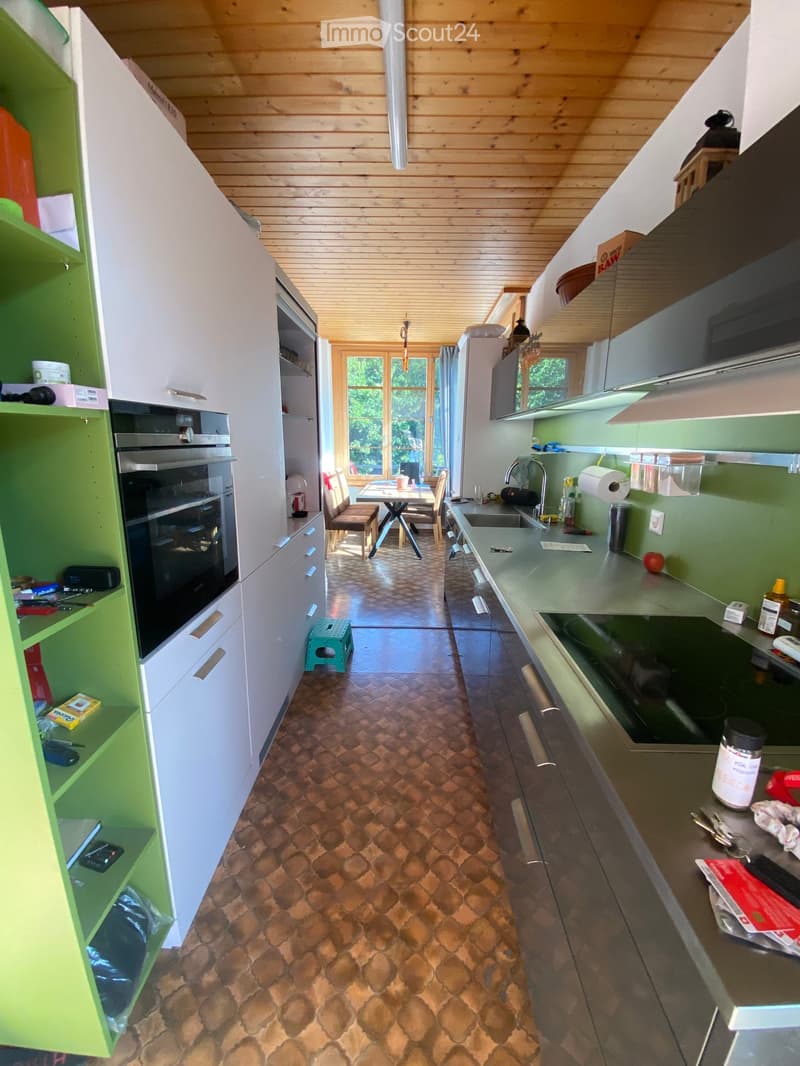 Modern kitchen with wooden ceiling, green and white cabinets, stainless steel appliances, and a dining area with a table and chairs.