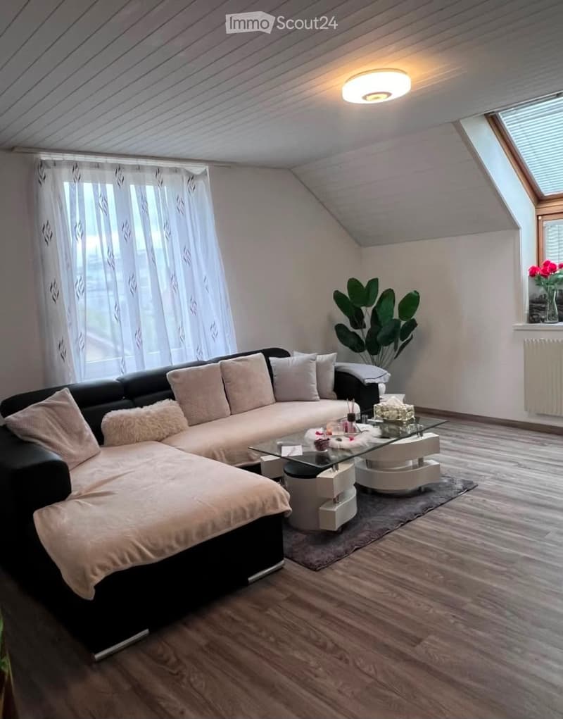 Modern living room with a black sectional sofa, glass coffee table, floor lamp, and large window with white curtains.