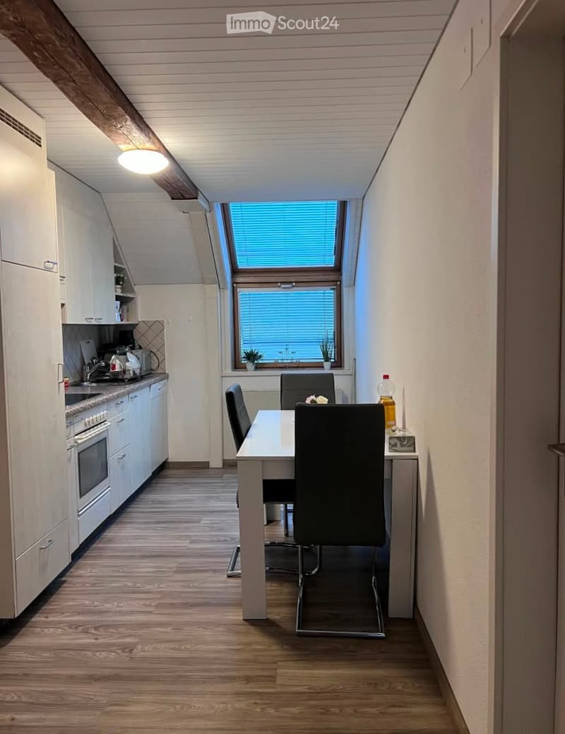 Modern kitchen and dining area with white cabinets, wooden flooring, and a large window with blinds. Includes a dining table with chairs, an oven, and a refrigerator.