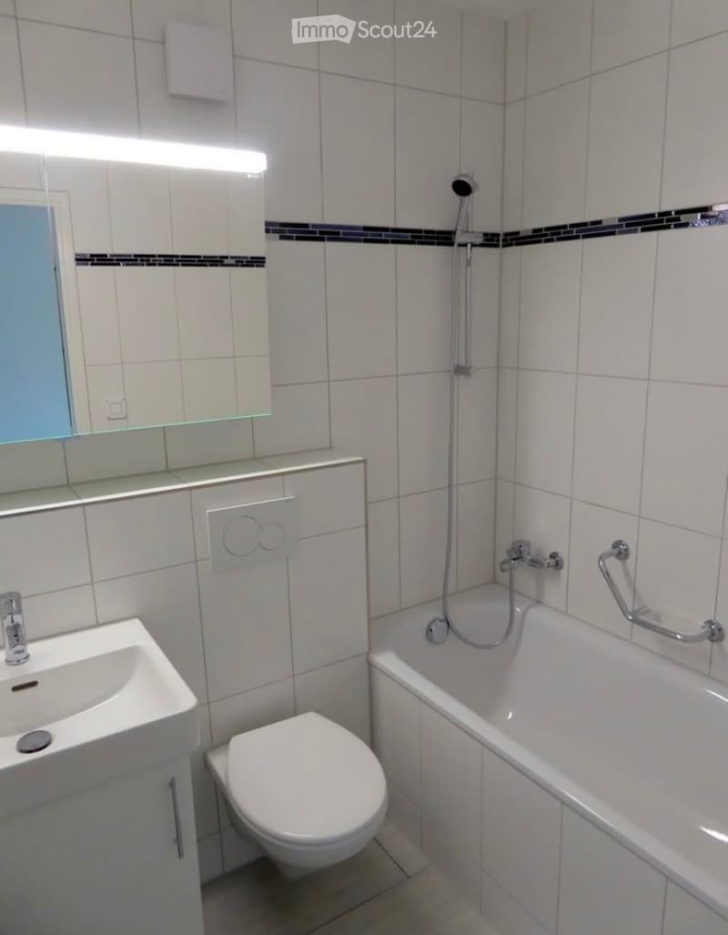 Modern bathroom with white tiles, a sink, toilet, bathtub, and a mirror above the sink.