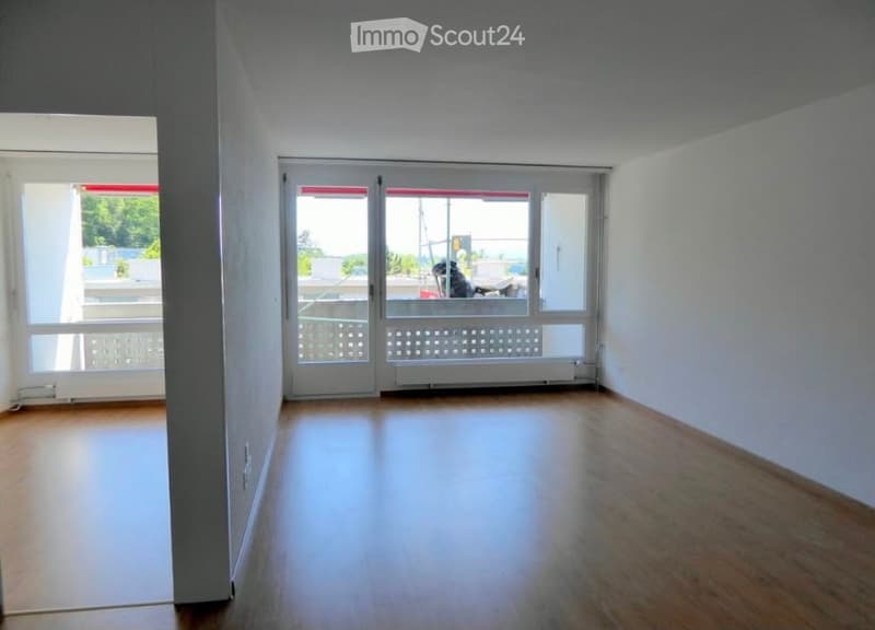 Empty room with wooden flooring, large windows, and a sliding glass door leading to a balcony.