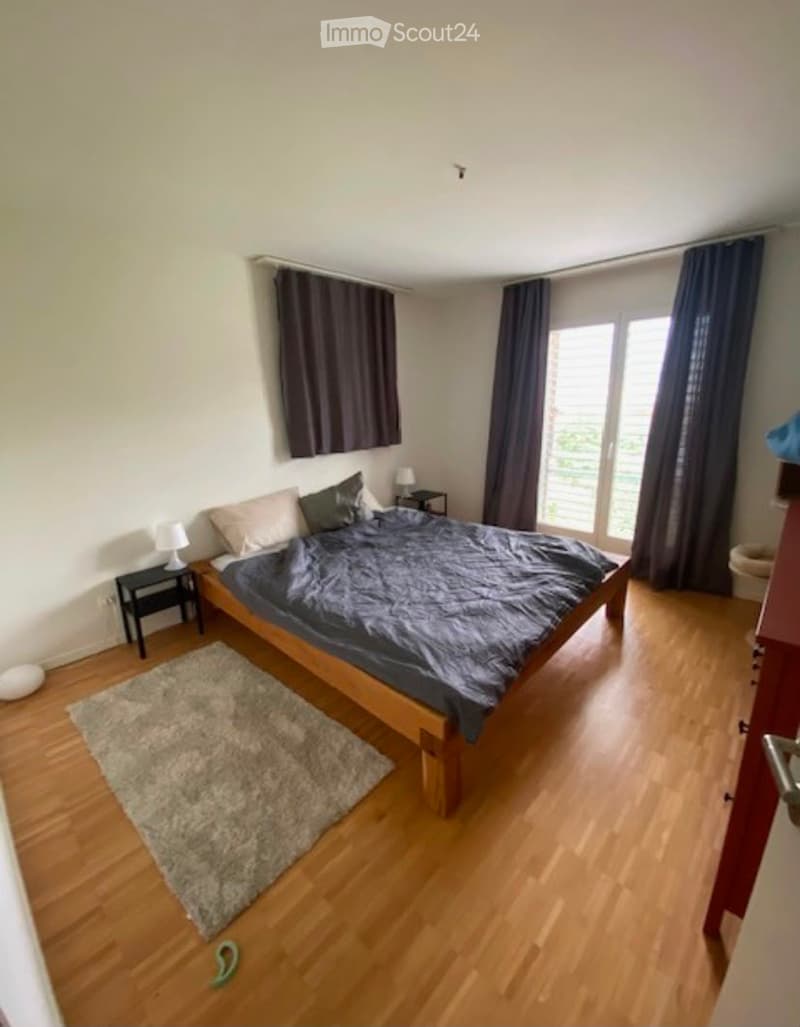 Cozy bedroom with wooden flooring, a large bed with pillows and blankets, nightstands with lamps, and a rug on the floor.
