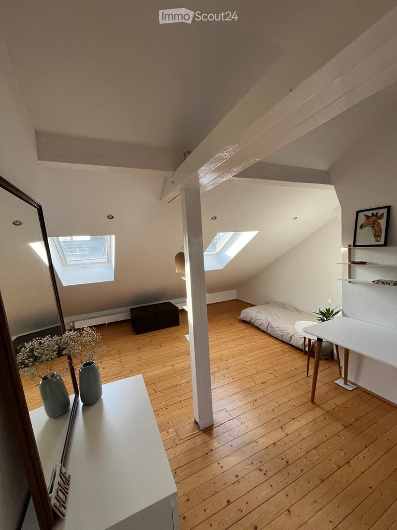 Loft-style room with wooden flooring, slanted ceilings, skylights, a small bed, a table with stools, shelves, and decorative vases.
