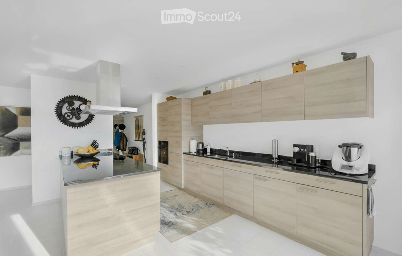Modern kitchen with light wood cabinets, black countertops, and stainless steel appliances. Features include a central island, a sink, and various kitchen appliances.