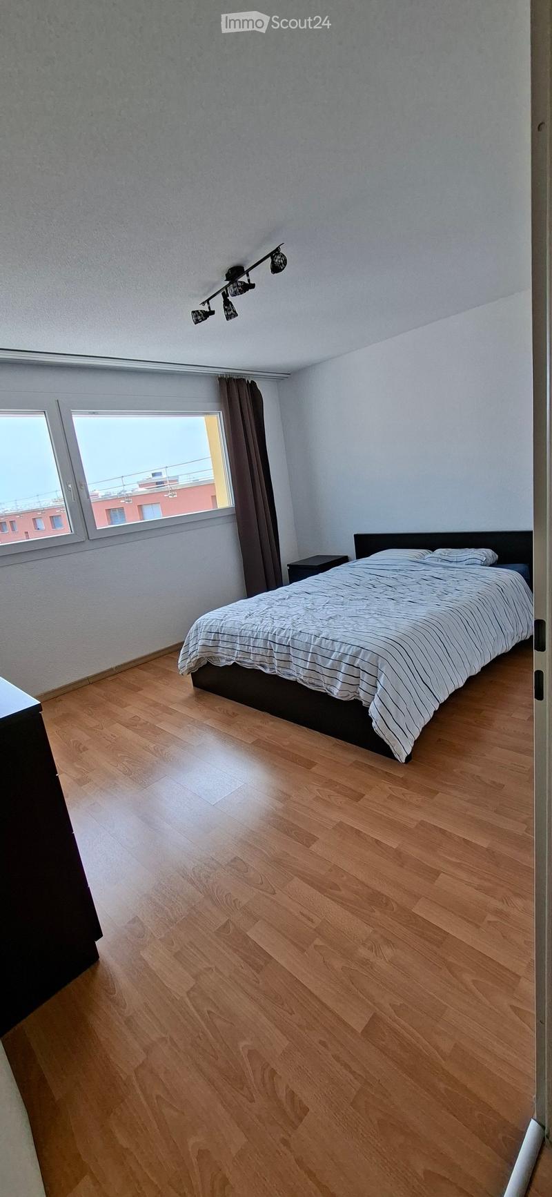 Bedroom with wooden flooring, a bed with striped bedding, a nightstand, and a window with curtains.