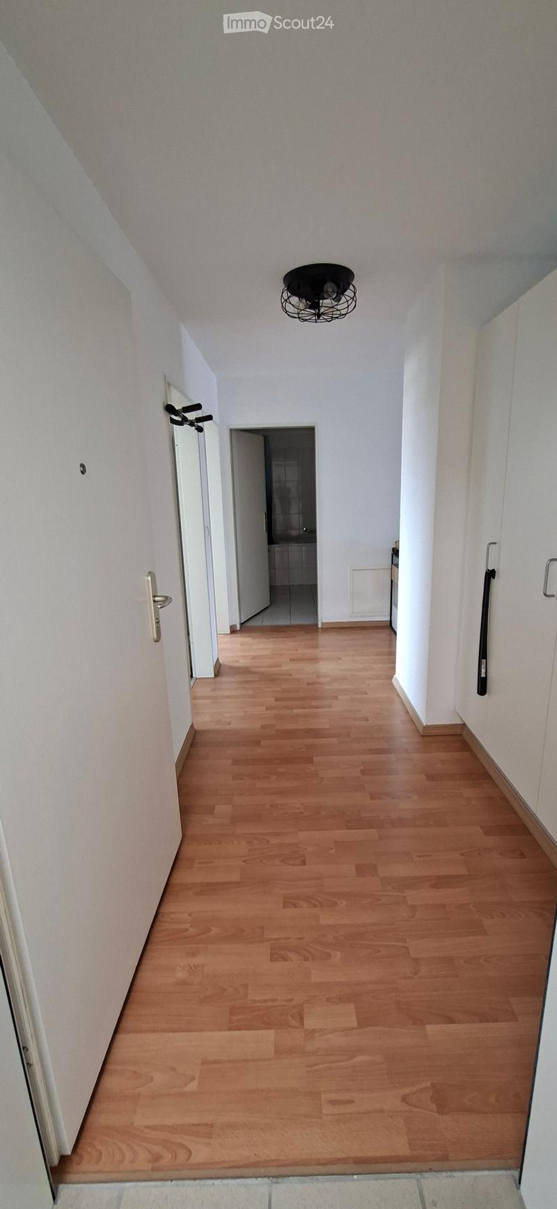 Empty hallway with wooden flooring, white walls, and a black hanging light fixture. Doors lead to adjacent rooms.