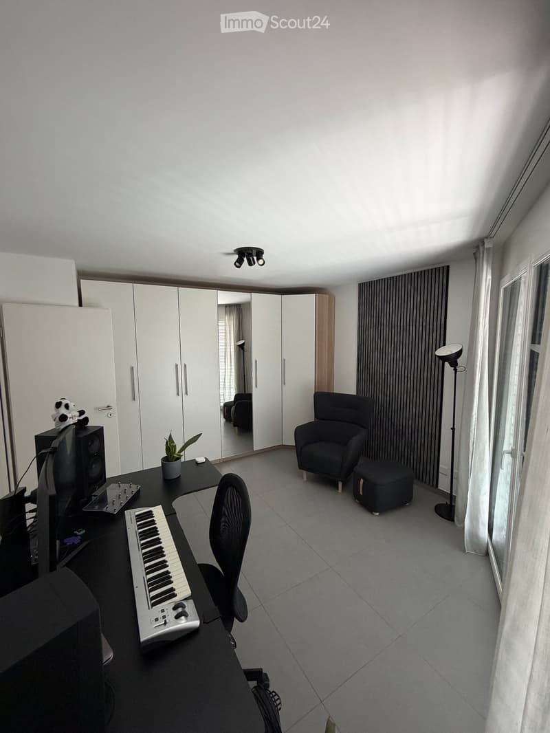 Modern, well-lit room with a desk, keyboard, chair, sofa, plant, mirror, wardrobe, and lamp.