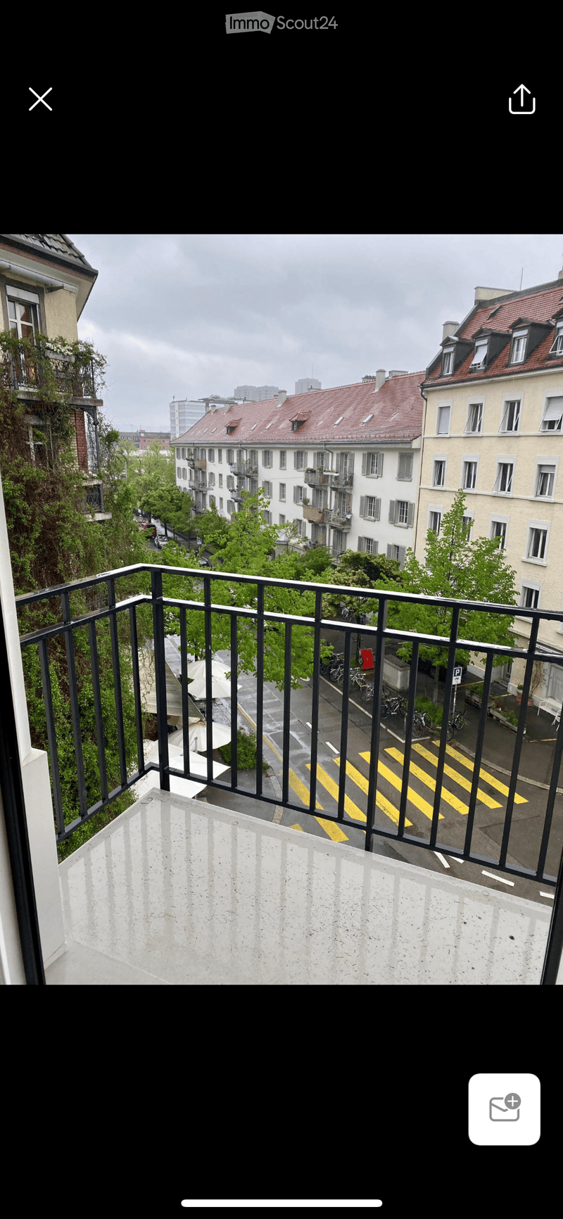 Balcony overlooking a city street with buildings, trees, and bicycles parked along the sidewalk.