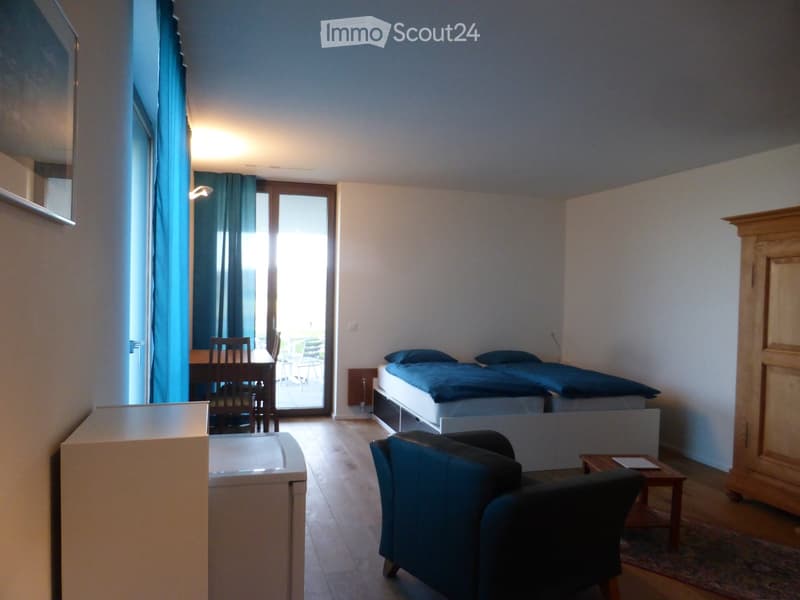 Brightly lit room with wooden flooring, two single beds, a sofa, a small table with chairs, and a wardrobe.