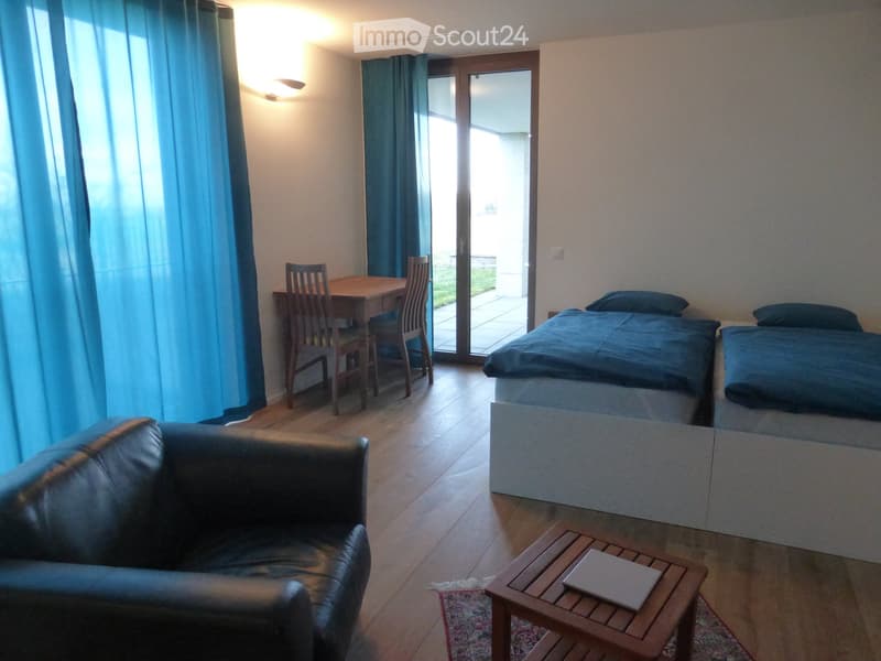 Cozy furnished room with a sofa, coffee table, laptop, dining area with a table and chairs, and a double bed with pillows.